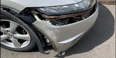Front corner of a silver car with accident damage to the bumper and headlight