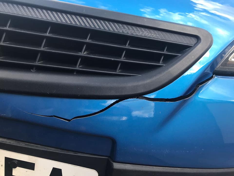 Cracked front bumper panel beside the grille on a blue car before repair