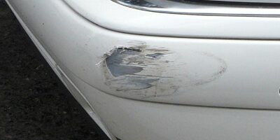 Scuffed and cracked corner of a white car bumper
