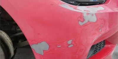 Red car bumper with paint damage showing filler