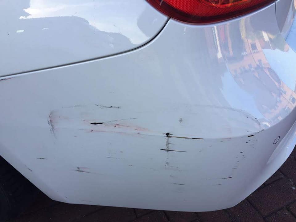 Scuffs and scratches across the rear bumper corner of a white car before repair